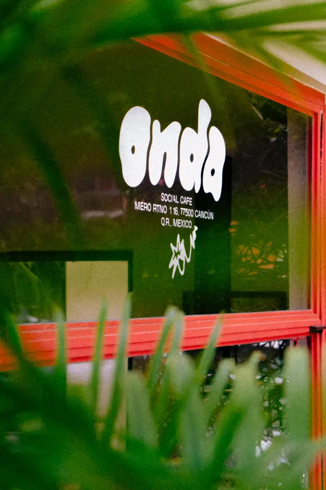 Logo de Onda Café en la ventana, enmarcado entre palmas